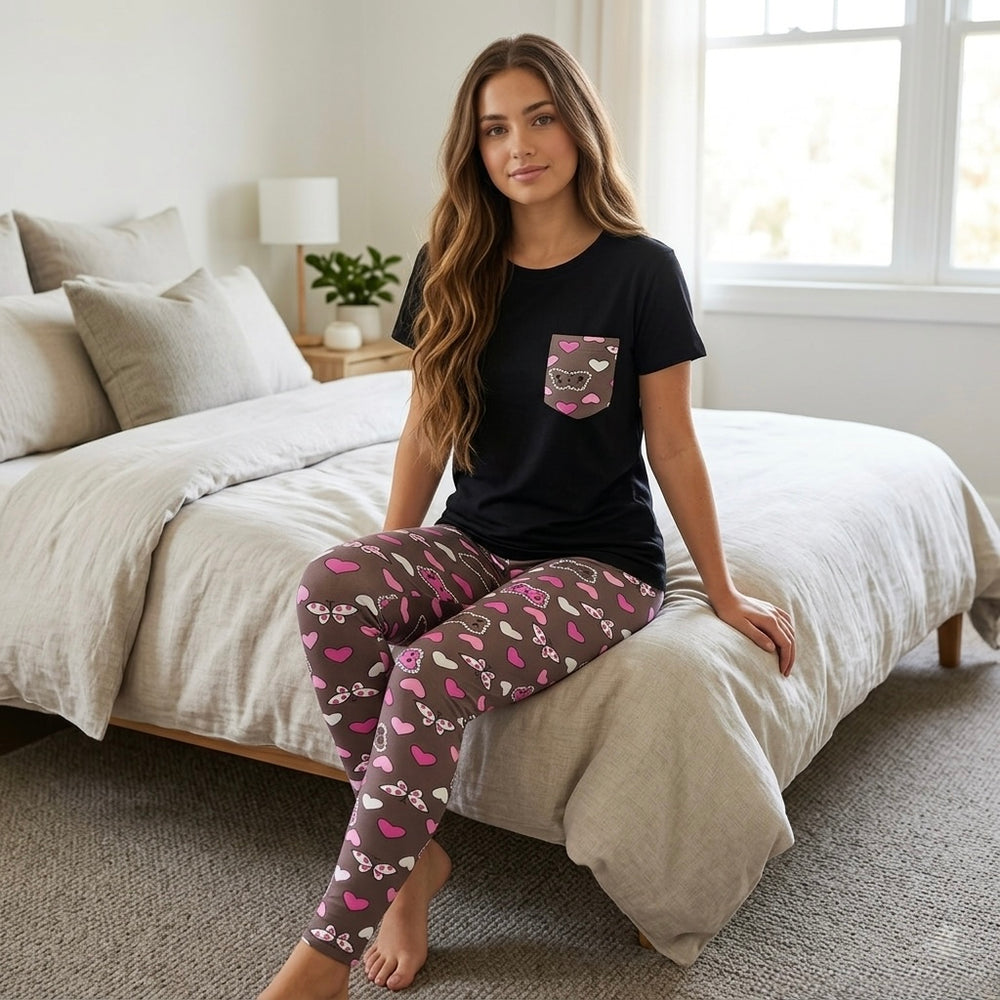 موديل ترتدى بيجامة قطن بنطلون مطبوع قلوب مع تيشيرت اسود ساده جالسة على السرير فى غرفة نوم بإضاءة طبيعية