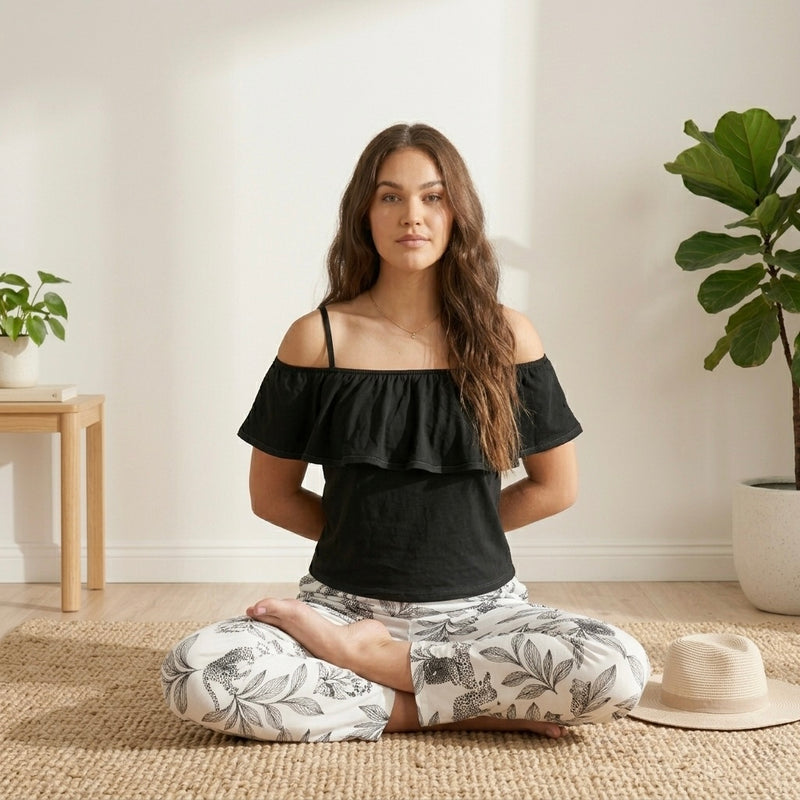 موديل جالسة على الأرض ترتدى بيجامة قطن مريحة بكروب توب أسود وبنطلون مطبوع بنقشة نباتية