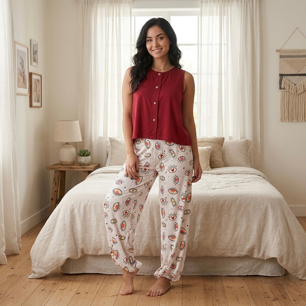موديل ترتدى بيجامة قطن مكونة من تيشيرت أحمر بدون أكمام وبنطلون مطبوع جالسة فى غرفة نوم بإضاءة طبيعية