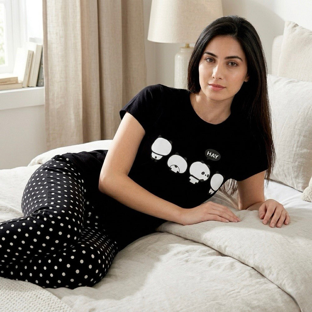 موديل ترتدى بيجامة قطن تركي سوداء بنطلون منقط وتيشيرت مطبوع مستلقية على السرير في غرفة نوم هادئة