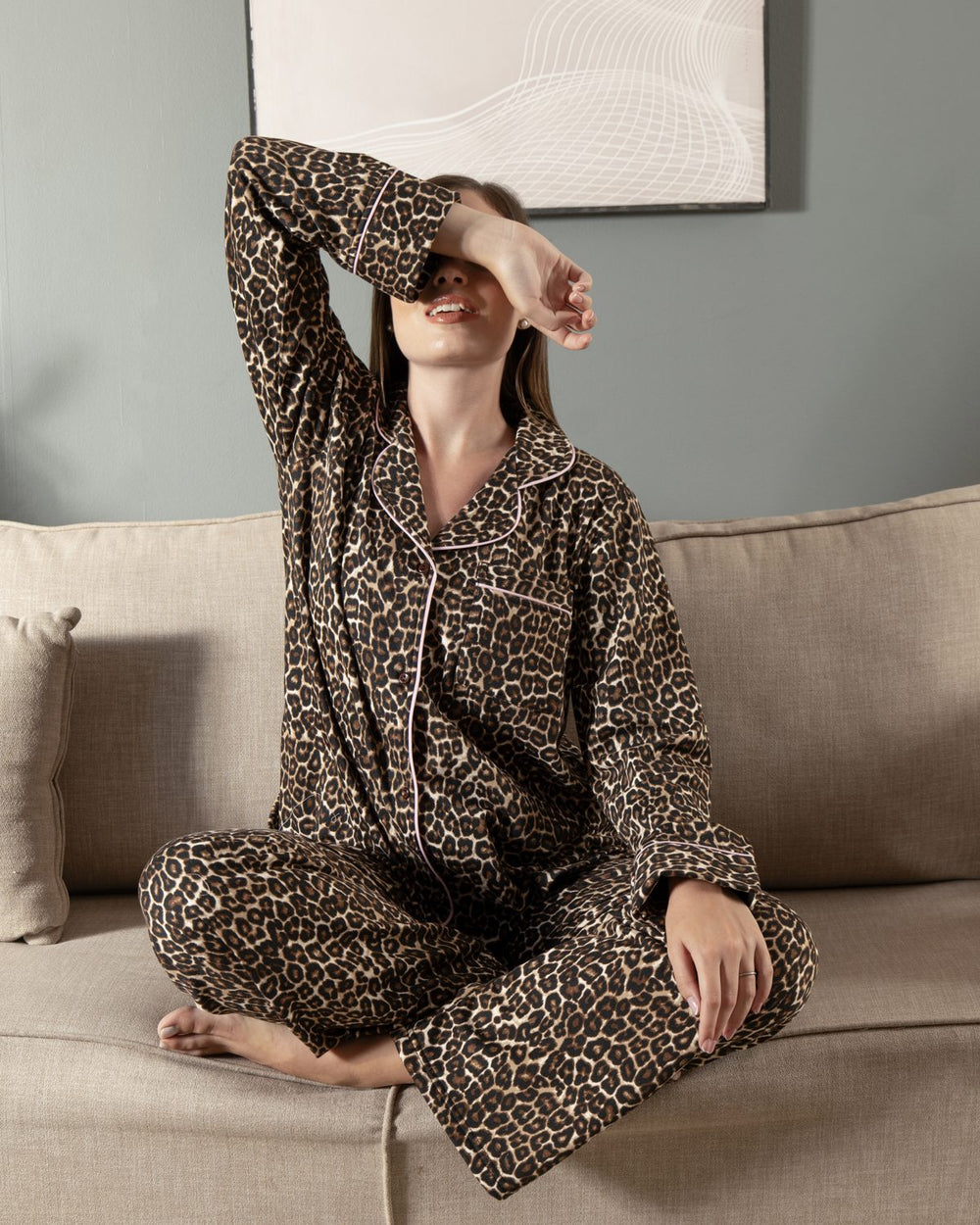 بيجامة Leopard Classic شتوية من PYJAMODA بنقشة ليوبارد بني، قميص بأزرار أمامية وبنطلون طويل، الموديل جالسة على الكنبة